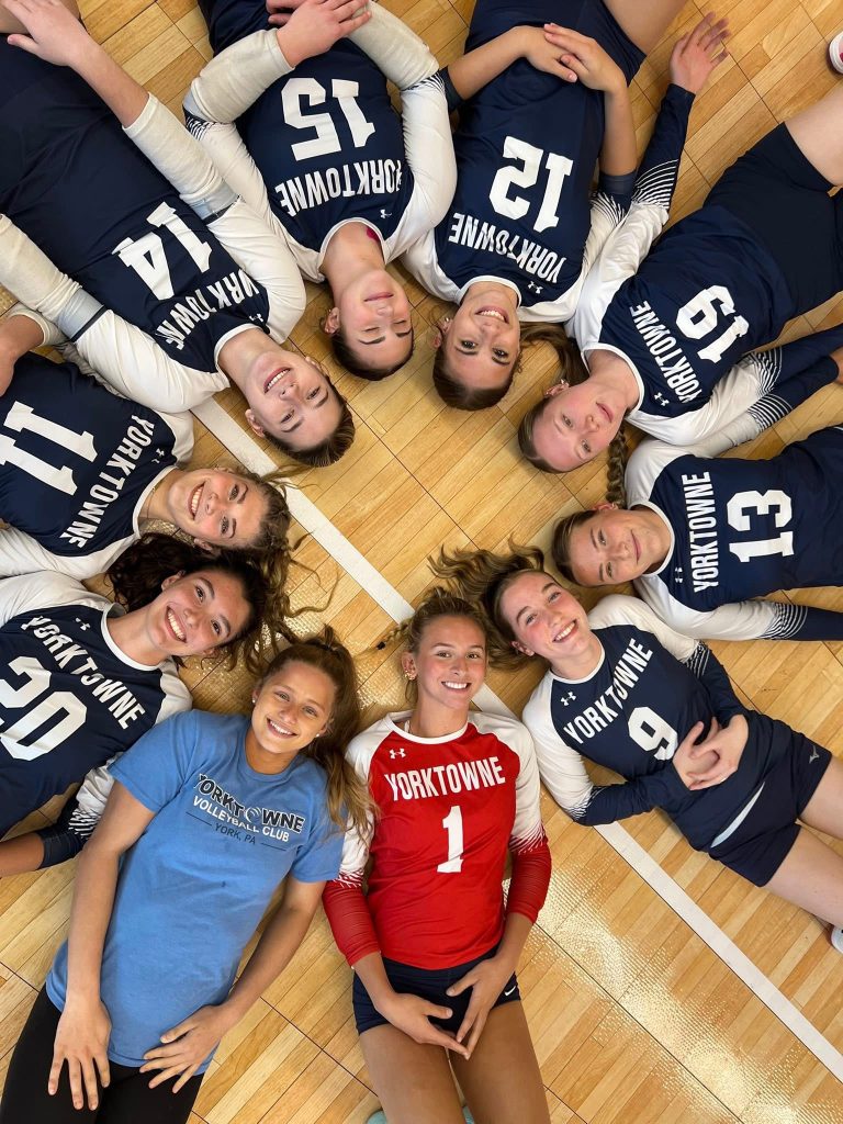 Yorktowne volleyball athletes in a team huddle on the court